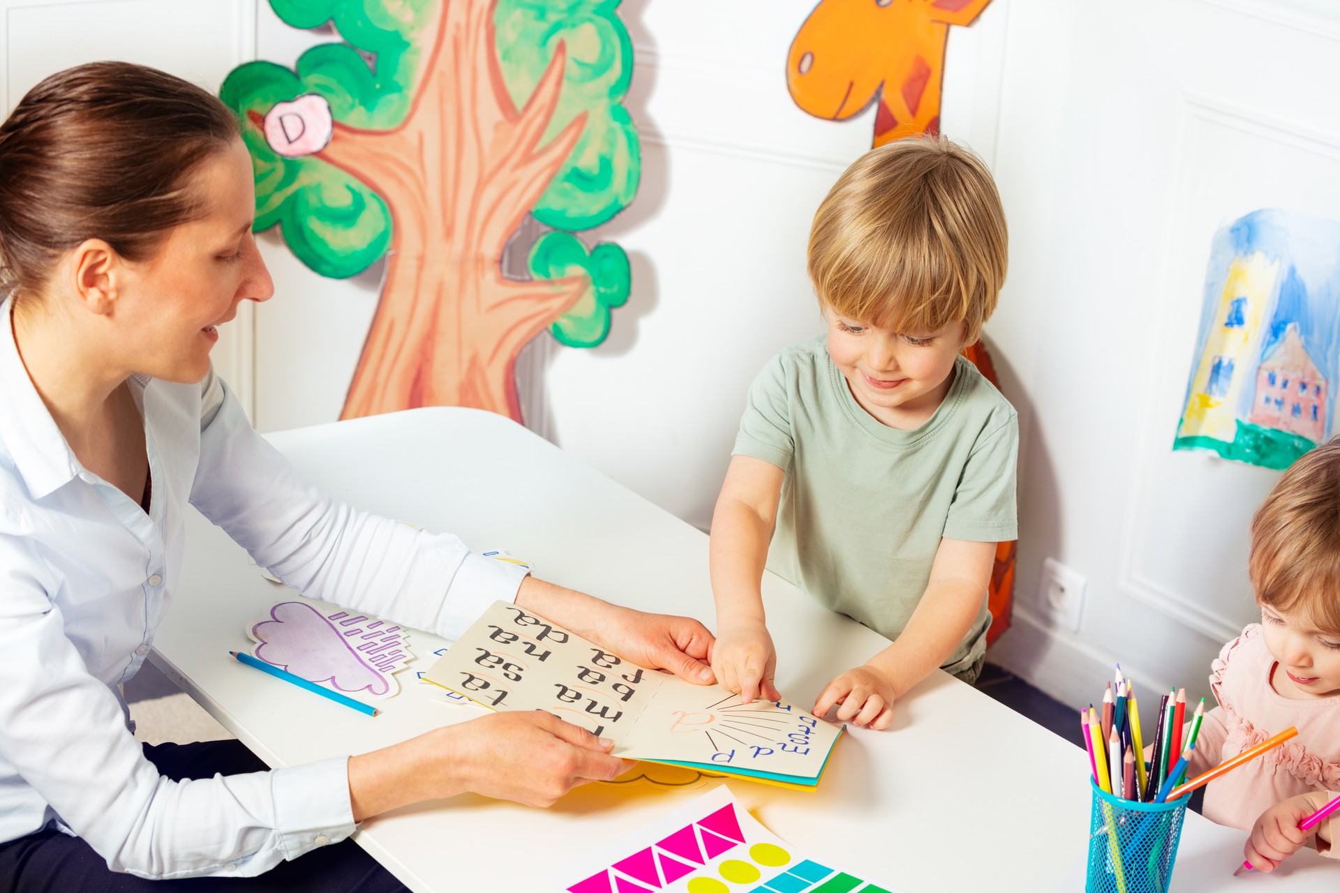 Woman teaches little kids to read letters in the book